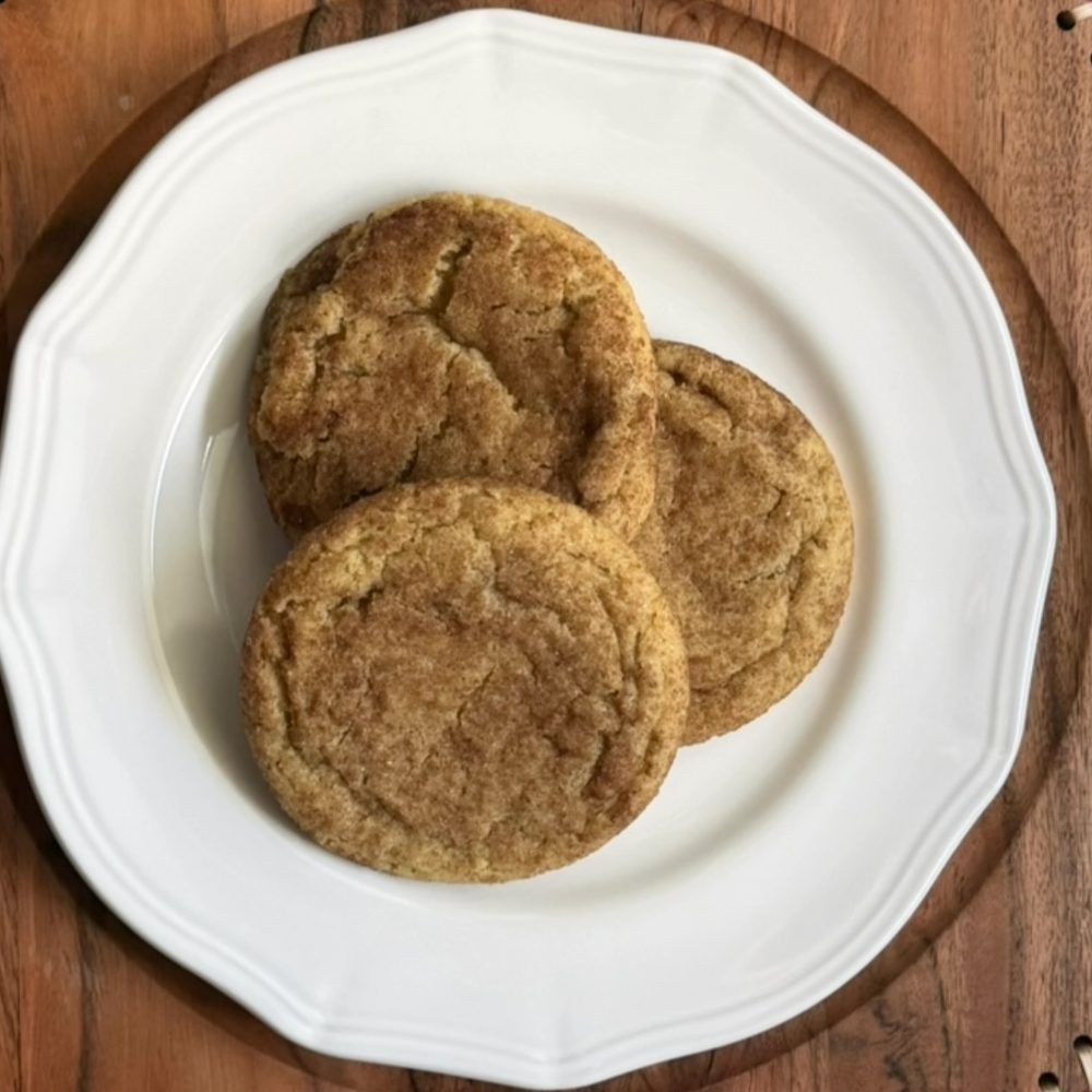 Three Snickerdoodle cookies with a crackly cinnamon-sugar top on a white plate